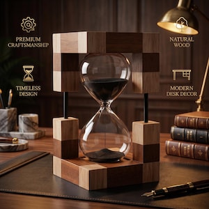 May include: An hourglass with a clear glass bulb containing black sand, set within a square frame constructed from alternating light and dark wood blocks. The frame is supported by thin black vertical rods, creating a geometric structure.