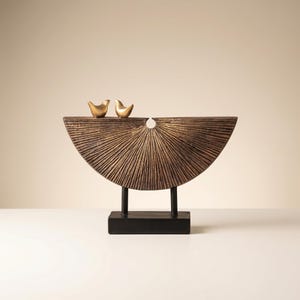 Può includere: Scultura decorativa color bronzo con design a semicerchio e linee radiali, sostenuta da supporti neri e base rettangolare. Due piccole statuette di uccelli dorati sulla parte superiore. Adatta per l'arredamento della casa.