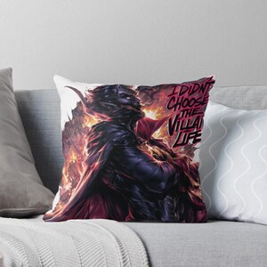 Peut inclure: Coussin avec une illustration dramatique d'un personnage sombre avec des accents rouges et des flammes. Le texte "I DIDN'T CHOOSE THE VILLAIN LIFE" est en rouge. Le coussin est sur un canap&eacute; gris.