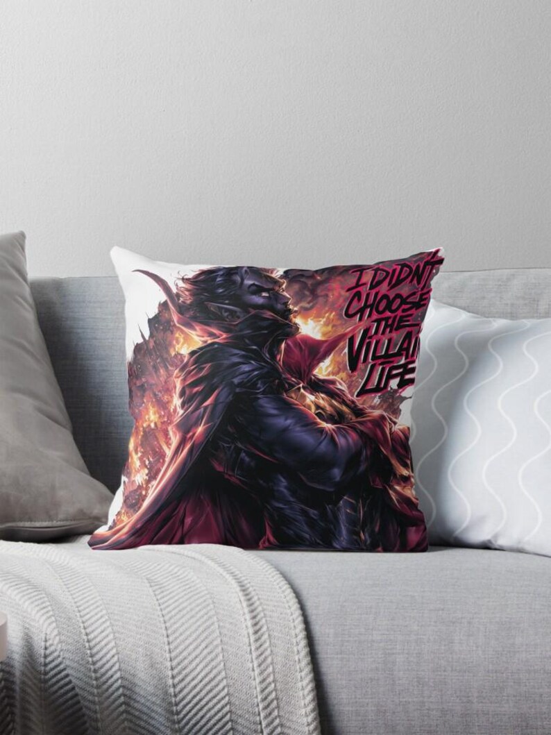 Peut inclure: Coussin avec une illustration dramatique d'un personnage sombre avec des accents rouges et des flammes. Le texte "I DIDN'T CHOOSE THE VILLAIN LIFE" est en rouge. Le coussin est sur un canap&eacute; gris.