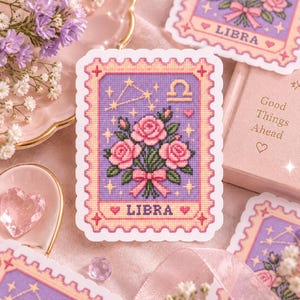 May include: A rectangular sticker shaped like a postage stamp featuring a purple background with a central bouquet of pink roses tied with a pink ribbon. The design includes a gold Libra zodiac symbol, a constellation, and the text LIBRA.