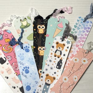 Puede incluir: Una colección de marcapáginas coloridos con varios diseños, incluyendo gatos, huellas de patas, búhos, una rana, un helado, un oso de peluche, margaritas y corazones. Cada marcapáginas tiene una cinta decorativa.