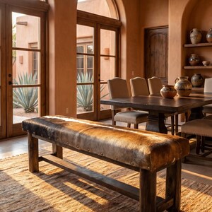 May include: A rectangular bench featuring a brown and black cowhide upholstered seat with brass nailhead trim, supported by four dark wooden legs connected by a horizontal stretcher bar, positioned in a room with arched windows and doorways.