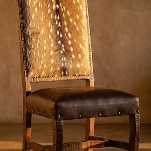 May include: A wooden chair featuring a high backrest upholstered in brown and white spotted animal hide. The seat is covered in smooth dark brown leather, accented with metal nailhead trim along the edges of both the seat and the backrest.