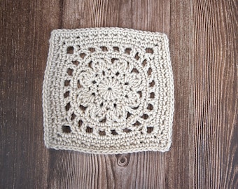 May include: A beige crocheted square with a detailed floral pattern in the centre.