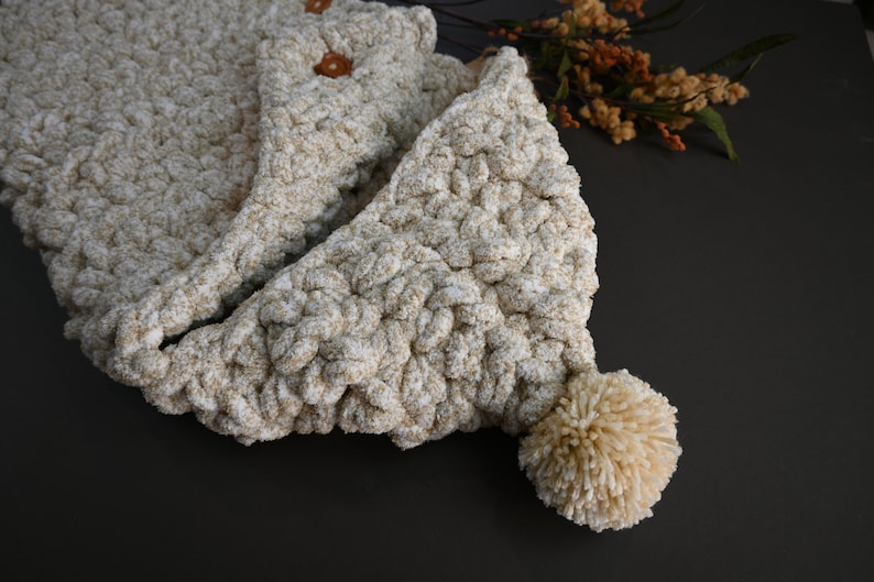 Pu&ograve; includere: Una sciarpa con cappuccio in crochet beige con un pompon soffice all'estremit&agrave;. La sciarpa &egrave; realizzata con un filato spesso e ha un aspetto testurizzato.