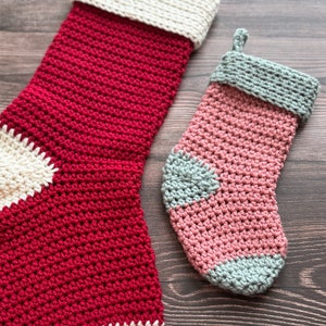 May include: Two crocheted Christmas stockings, one red and white and one pink and gray.