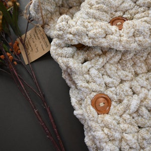 Pu&ograve; includere: Una coperta all'uncinetto color crema con due bottoni in legno. La coperta &egrave; realizzata con un filato spesso e ha una texture morbida e soffice.