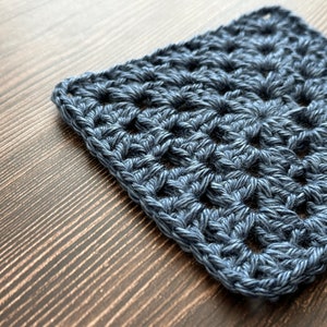 May include: A close-up of a blue crocheted square with a repeating pattern of holes.