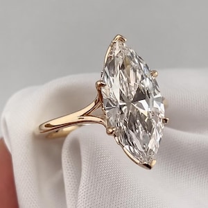 Peut inclure: Une bague avec une pierre précieuse transparente taille marquise montée sur un anneau en or poli. La pierre est maintenue par six griffes et l'anneau présente un design à tige fendue là où le métal rencontre le sertissage, offrant un aspect élégant.