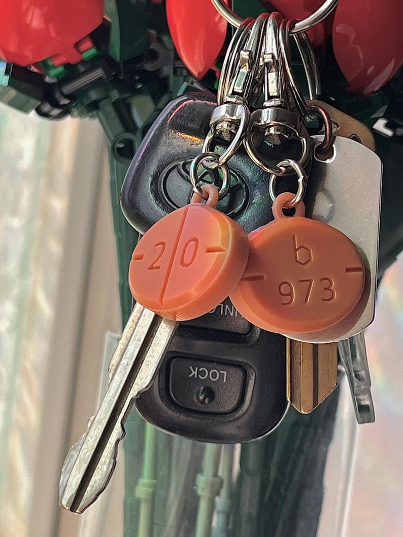 May include: A collection of keys and keychains. Two orange keychains with the numbers "20" and "973" are attached to keys and a car remote. The keys are on a silver keyring. The background is blurred.