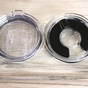 May include: Two clear plastic lids for a travel mug. One lid has a black silicone ring around the opening. The other lid has a clear plastic slider.