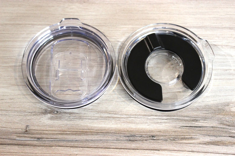 May include: Two clear plastic lids for a travel mug. One lid has a black silicone ring around the opening. The other lid has a clear plastic slider.
