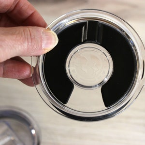 May include: A clear plastic lid with a black rubber seal and a small silver logo. The lid has a lip around the edge and a small handle on the side.