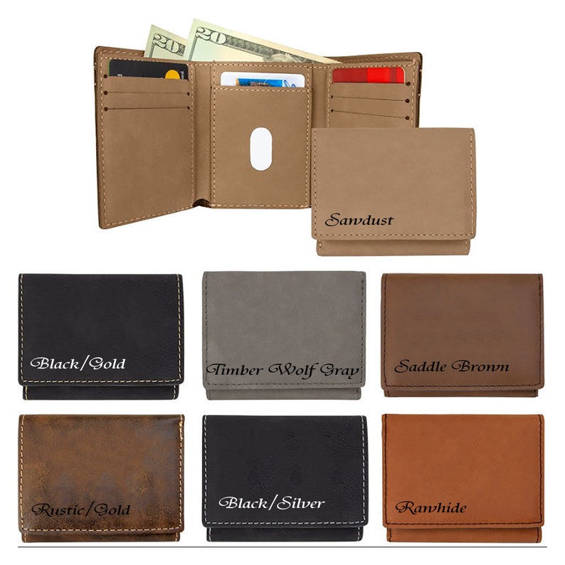 May include: A collection of trifold wallets in various colors including black, gray, brown, and rustic tan. Each wallet features visible stitching and engraved text labels such as Black/Gold, Timber Wolf Gray, Saddle Brown, Rustic/Gold, Black/Silver, and Rawhide.