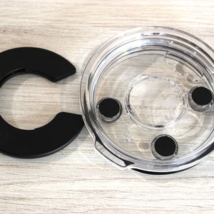 May include: A clear plastic lid with a black rubber ring and three black rubber feet. The lid is designed to fit on a container.