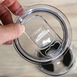 May include: A clear plastic lid with a black rubber seal and a sliding lid for a travel mug.