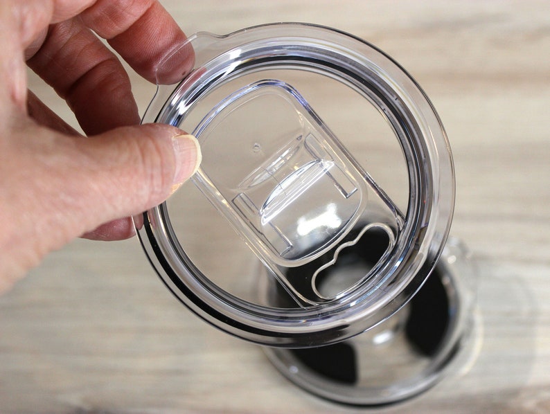 May include: A clear plastic lid with a black rubber seal and a sliding lid for a travel mug.