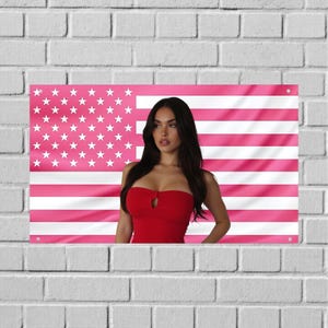 Puede incluir: Una bandera de pared rectangular con un diseño de bandera estadounidense rosa y blanca con una mujer con un top rojo sin tirantes. La bandera tiene estrellas blancas en la esquina superior izquierda y rayas rosas y blancas.