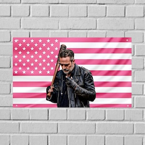 May include: A rectangular wall banner featuring a man with a beard wearing a black leather jacket and fingerless gloves, holding a baseball bat wrapped in barbed wire. The background is a pink and white version of the American flag with stars.