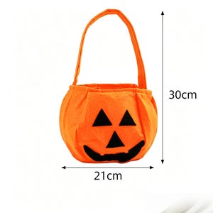 May include: An orange fabric pumpkin-shaped treat bag with a black felt jack-o'-lantern face featuring triangular eyes and a wide grin. The bag has a single handle and measures 30 cm in height and 21 cm in width as indicated by arrows.