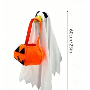 May include: A white ghost figure with black eyes and a yellow beak, holding an orange pumpkin-shaped trick-or-treat bag with black felt facial features. The figure measures 23 inches in height, as indicated by the vertical measurement marker.