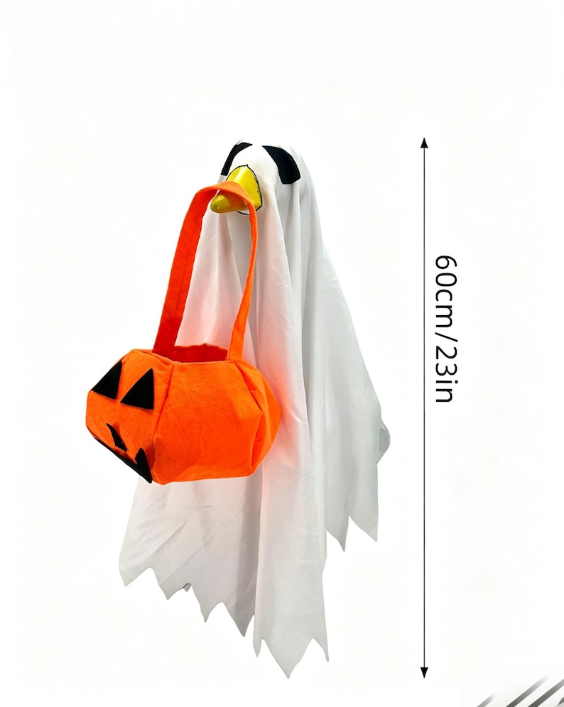 May include: A white ghost figure with black eyes and a yellow beak, holding an orange pumpkin-shaped trick-or-treat bag with black felt facial features. The figure measures 23 inches in height, as indicated by the vertical measurement marker.