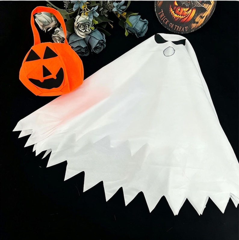 May include: A white ghost costume cape featuring a jagged hem and a printed face with black eyes and a circular mouth, paired with an orange pumpkin-shaped trick-or-treat bucket with a black jack-o'-lantern face and a handle.