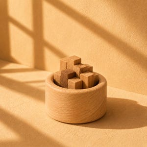 以下が含まれることがあります： 明るい色の木製の丸いボウルに、さまざまな茶色の色合いの小さな無垢の木製キューブが入っています。ボウルには滑らかな円形の縁と自然な木目があり、キューブは容器の中に積み重ねられています。