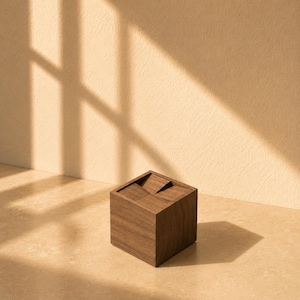 Pode incluir: Um cubo de madeira castanho-escuro com uma superfície superior rebaixada apresentando planos geométricos inclinados. O objeto tem um acabamento liso de grão de madeira natural e forma quadrada, apresentado como um bloco sólido com um entalhe.