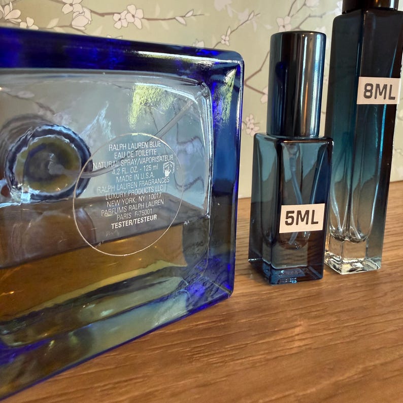 Pode incluir: Tr&ecirc;s frascos de perfume de vidro azul de tamanhos variados. O frasco maior tem formato quadrado e o texto "RALPH LAUREN BLUE EAU DE TOILETTE" &eacute; vis&iacute;vel. Os frascos menores est&atilde;o rotulados "5ML" e "8ML".