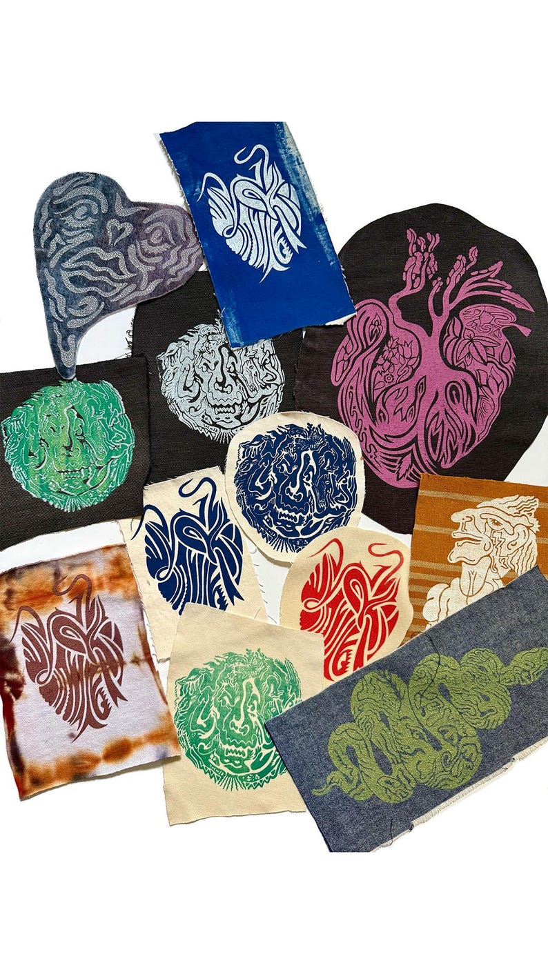 May include: A collection of fabric patches with various linocut designs. The patches feature images of faces, hearts, and abstract shapes in colors like blue, green, red, and brown. Some patches have a tie-dye effect.