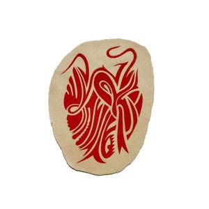 Puede incluir: Un parche ovalado beige con un llamativo diseño tribal rojo. El diseño se compone de líneas fluidas y formas estilizadas. Este parche podría usarse para decorar ropa o accesorios, agregando un elemento visual único.