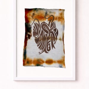 May include: Abstract artwork in a white frame. The art piece features a brown, stylized design on a tie-dye background with orange, brown, and blue hues. The artwork is a unique, decorative piece.