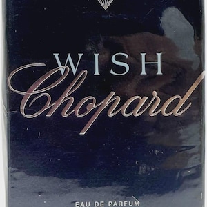 Peut inclure: Une boîte de parfum rectangulaire bleu foncé avec le texte WISH Chopard en lettres blanches et argentées. Une petite icône de diamant est centrée au-dessus du texte. Le bas indique EAU DE PARFUM NATURAL SPRAY 2.5 FL OZ 75 ml.