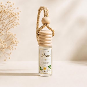 May include: A small glass car air freshener bottle with a frosted finish, topped with a light-colored wooden cap and a matching wooden bead. A braided cord is attached for hanging. The label reads Parfum Monoï Déodorant Voiture.