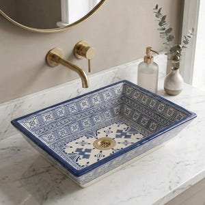 May include: A rectangular ceramic vessel sink featuring a white base with intricate blue geometric and floral patterns. The sink includes a gold-toned drain and is paired with a wall-mounted gold-toned faucet fixture above a white marble countertop.