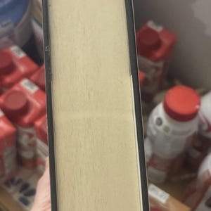 May include: A hardcover book with a light beige page block and a black spine. The pages are visible from the side, showing a textured surface. The book's edges are rounded.