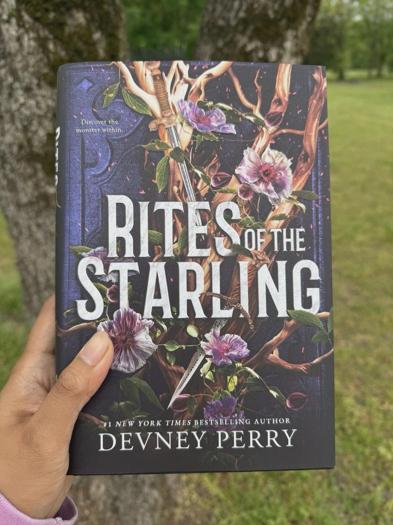 May include: A hardcover book titled "Rites of the Starling" by Devney Perry. The cover features a dark background with floral and vine illustrations, a sword, and the text "Discover the monster within."
