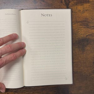 May include: Open notebook with lined pages and the word "NOTES" at the top. The book is open to a page with lines for writing. The book is on a wooden surface. The text "The Book of Enoch" is visible.