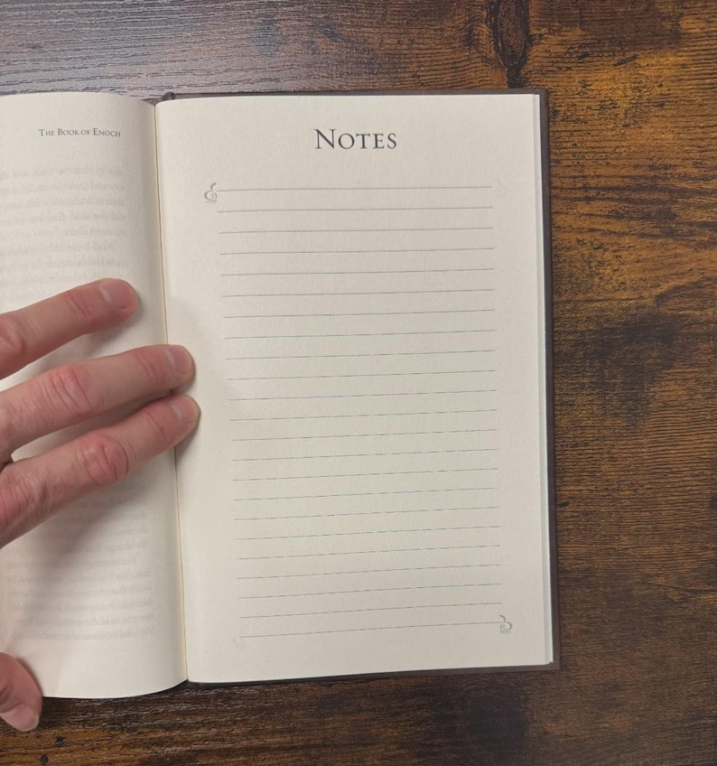 May include: Open notebook with lined pages and the word "NOTES" at the top. The book is open to a page with lines for writing. The book is on a wooden surface. The text "The Book of Enoch" is visible.
