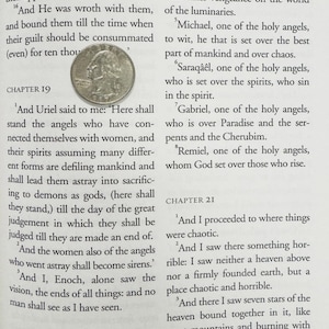 May include: A page from a book with printed text and a quarter coin. The text is divided into chapters and includes the names of angels. The quarter coin is in the center of the page.