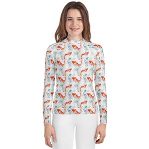 May include: A long-sleeved shirt featuring a repeating pattern of orange koi fish and blue aquatic plants on a white background. The shirt has a high neckline and is worn with white pants. The overall style is casual and aquatic-themed.