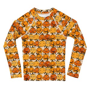 May include: A long-sleeve shirt featuring a repeating pattern of orange and yellow cartoon pumpkins with various facial expressions on a light beige background. The design includes small black text that reads "Boo" and "He-He" scattered among the pumpkins.
