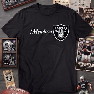 May include: Black t-shirt with the word "Mendoza" in white script and a Raiders logo. The image includes football memorabilia, including a football, miniature helmets, and a figurine of a football player.
