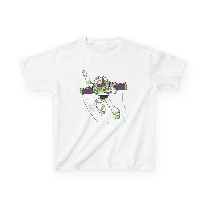 Puede incluir: Camiseta blanca con una ilustraci&oacute;n de dibujos animados de Buzz Lightyear en vuelo. El personaje se muestra con su traje de guardi&aacute;n espacial, con detalles verdes, morados y blancos. L&iacute;neas negras sugieren movimiento.