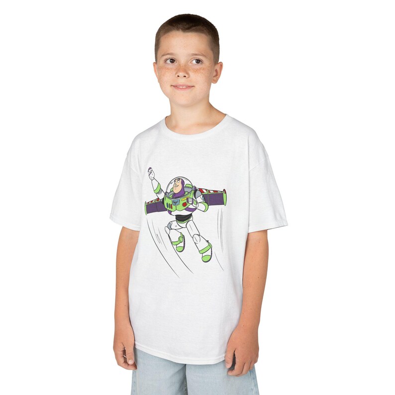 Puede incluir: Camiseta blanca con una ilustraci&oacute;n de dibujos animados de Buzz Lightyear en vuelo. El personaje est&aacute; representado con su traje de guardabosques espacial, con detalles verdes, morados y blancos. La camiseta es de estilo cuello redondo cl&aacute;sico.