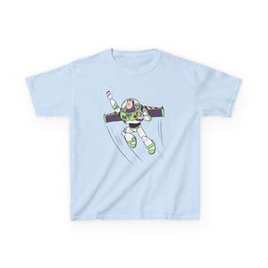 Puede incluir: Camiseta azul claro con una ilustraci&oacute;n de dibujos animados de Buzz Lightyear en pleno vuelo. El personaje lleva su traje de guardabosques espacial, con detalles verdes, blancos, morados y rojos. La camiseta es de tejido suave.