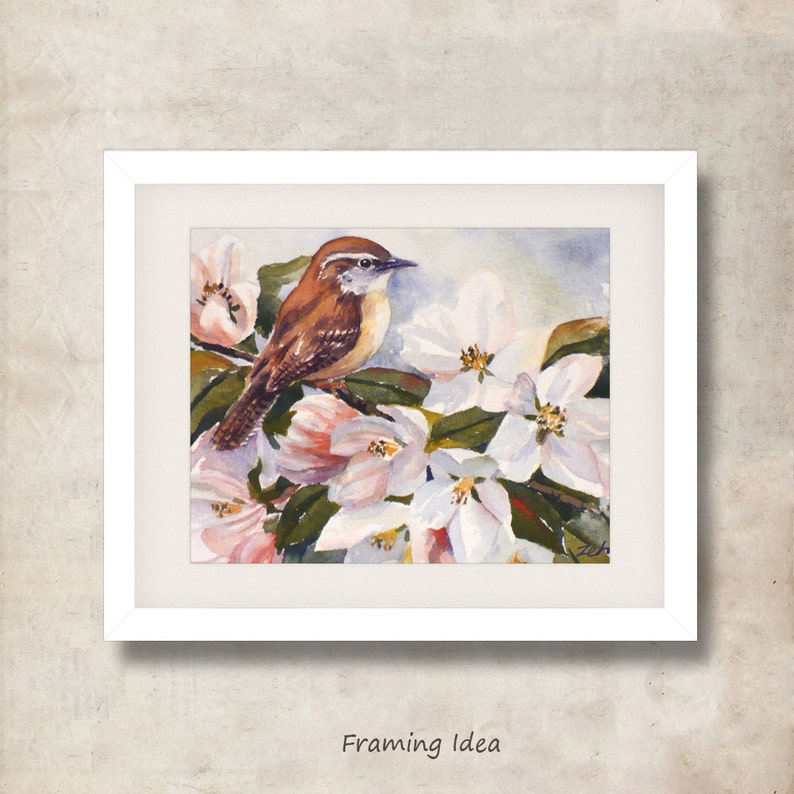 May include: Watercolor painting of a small brown bird perched on a flowering branch with white and pink blossoms. The artwork is framed in a white mat and frame. The text "Framing Idea" is at the bottom of the image.