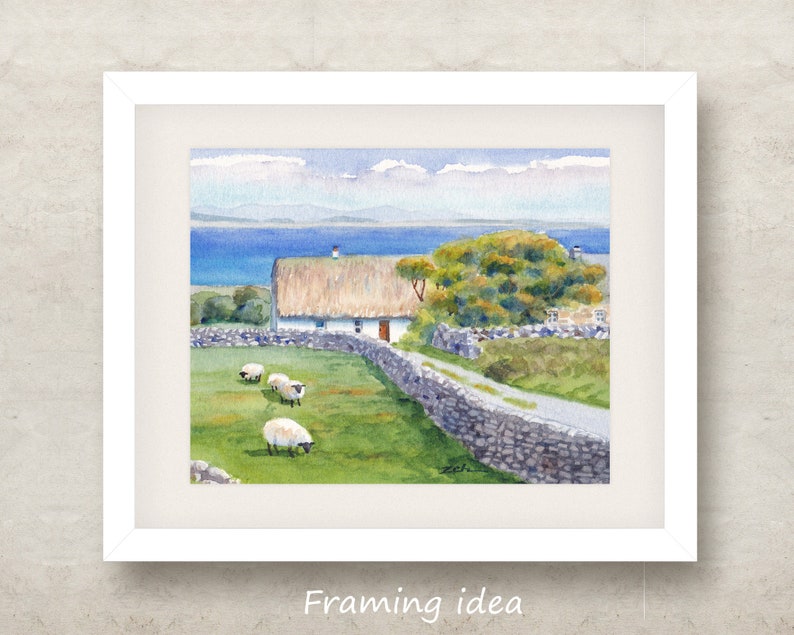 May include: Watercolor painting of a rural landscape with a white cottage, thatched roof, and stone wall. Sheep graze in a green field. The background features a blue sea and sky. The painting is framed in a white border.